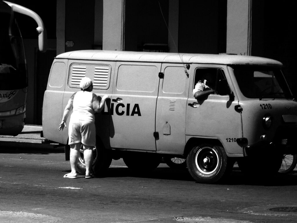 Mujer vestida de blanco trata de mirar por una rejilla de una furgoneta de la policía cubana.