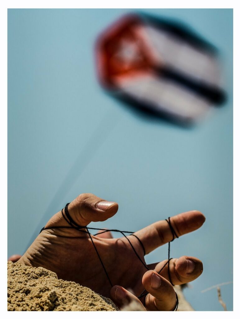 Dedos enredados con hilos de un papalote que es la bandera cubana.