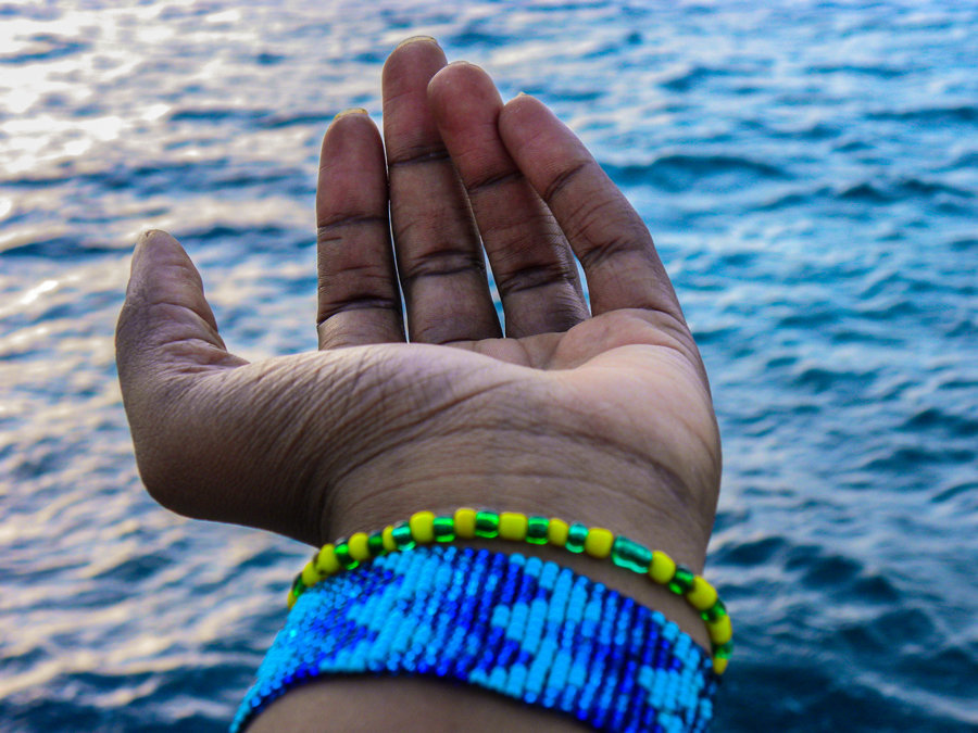 Primer plano de una mano de mujer negra con pulsos de religión afrocubana, abierta ante el mar.