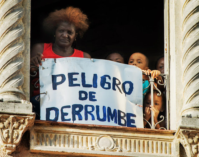 Mujer y muchos niños en un balcón con un cartel que dice "peligro de derrumbe".
