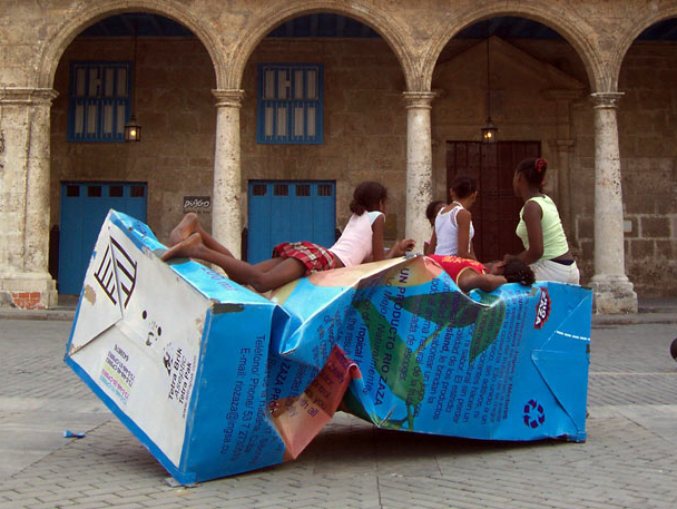 Niñas acostadas sobre una escultura que es una caja de jugo gigante.