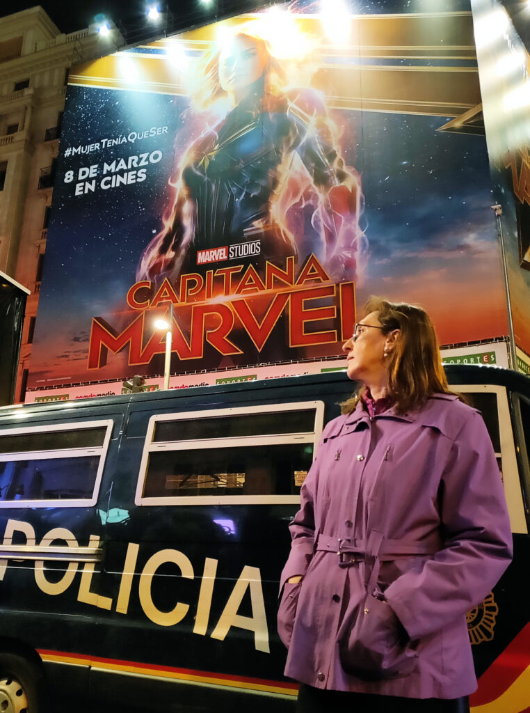 Mujer ante carro de policía y cartel de película.