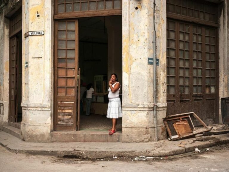 Mujer parada en la puerta de un edificio deteriorado en La Habana.