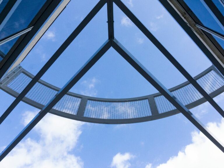 Cielo azul visto a través de rejas y cristales, forma un triángulo que recuerda la forma de una casa.