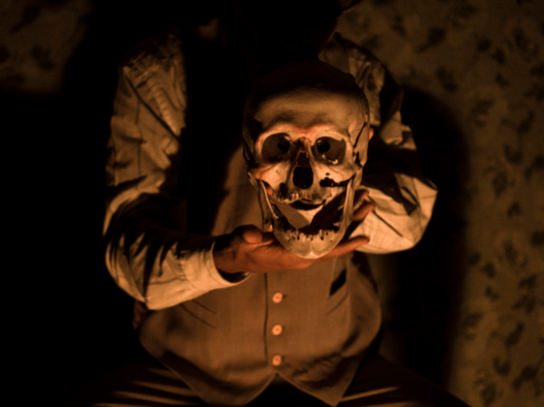 Actor sosteniendo una máscara en la obra "Hojas de Hierba", puesta en escena basada en la poesía de Walt Whitman.