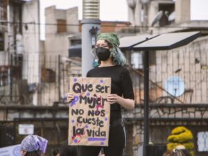 Mujer manifestándose con un cartel que denuncia el feminicidio: "Que ser mujer no nos cueste la vida".