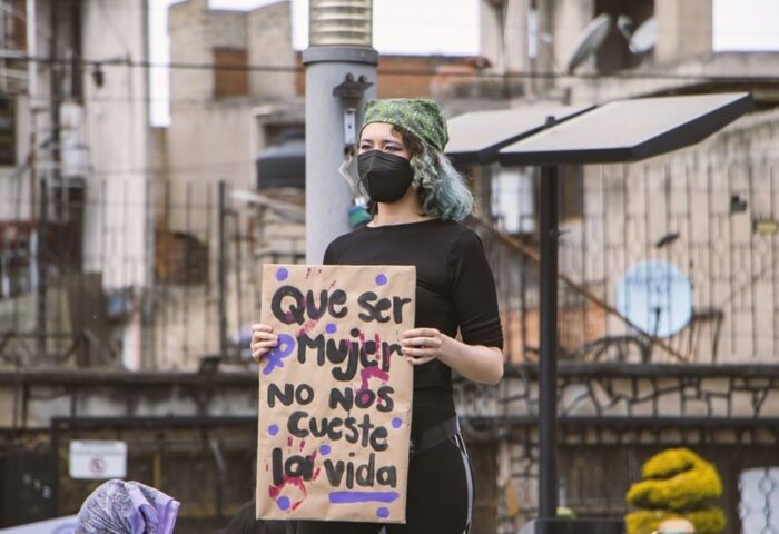 Mujer manifestándose con un cartel que denuncia el feminicidio: "Que ser mujer no nos cueste la vida".