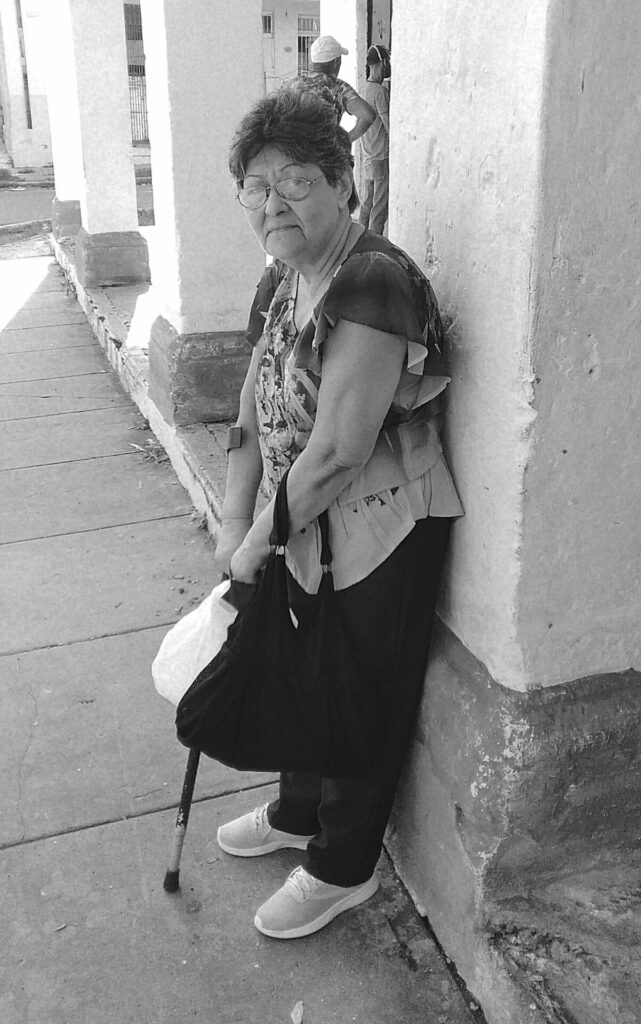 Anciana con bastón recostada a una columna.