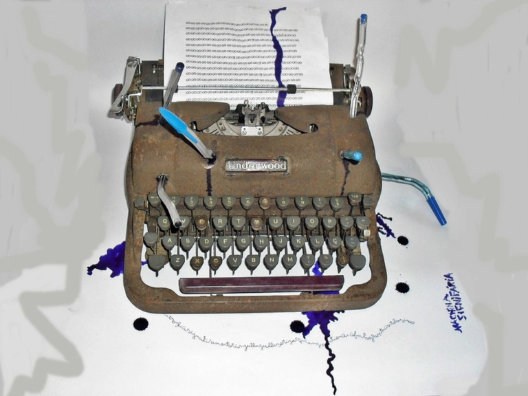 Máquina de escribir con tinta, papel y bolígrafo alrededor y encima.