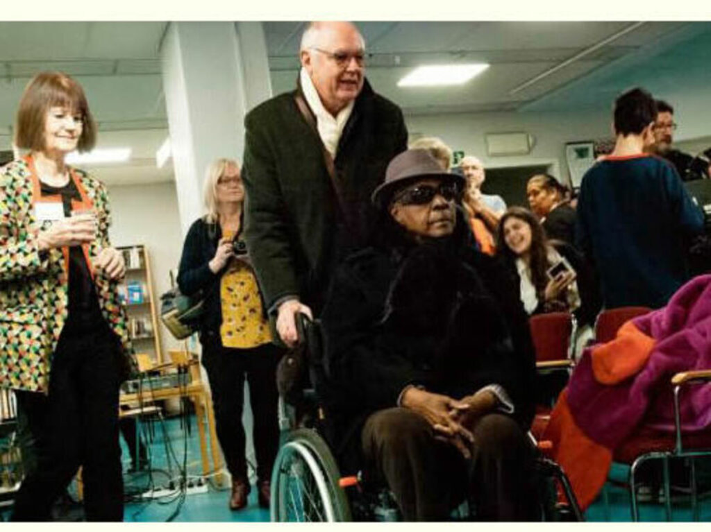 Maryse Condé, en silla de ruedas, es llevada por Richard Philcox, su traductor y compañero de vida.