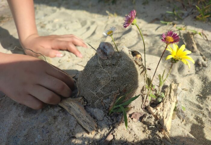 Castillo de arena con flores y manos de niño.