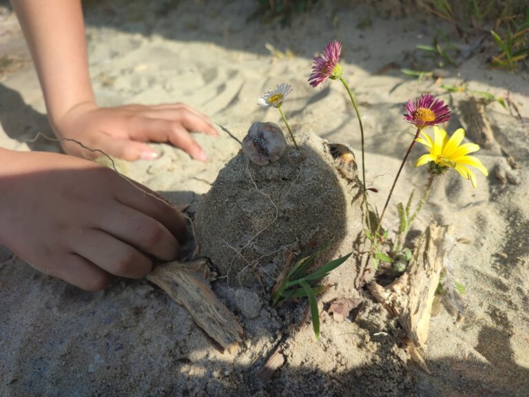 Castillo de arena con flores y manos de niño.