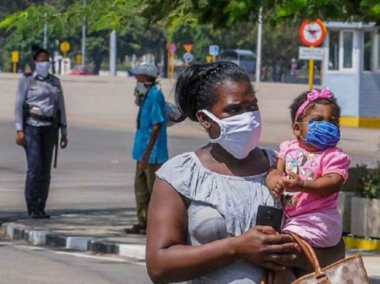 Madre cubana llevando a su bebé en brazos. Detrás una policía.