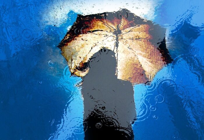 Reflejo en el agua de una mujer bajo la lluvia con sombrilla.