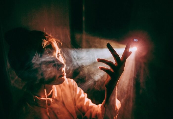 Mujer pone sus dedos entre un rayo de luz que entra en una habitación oscura.
