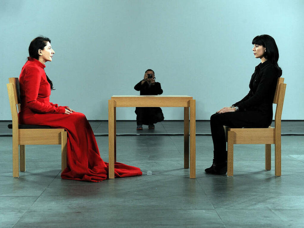 Abramovic en el performance "The Artist Is Present" (2010): sentada a la mesa con otra persona delante.