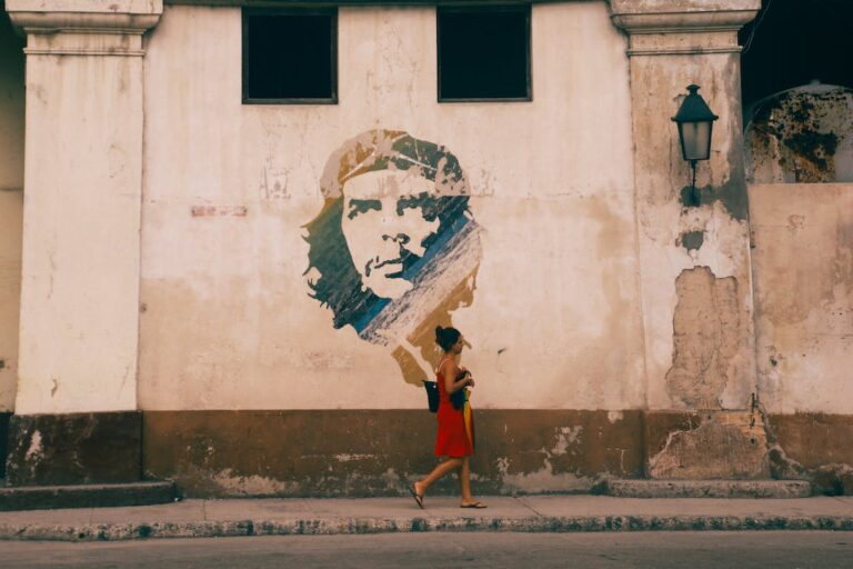 Fotografía de fachada cubana en ruinas con imagen de Che Guevara y chica pasando