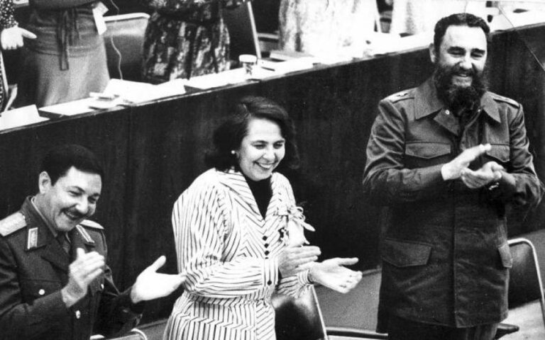 Fotografía donde aparecen Fidel y Raúl Castro, con Vilma Espín al centro, de pie, aplaudiendo.