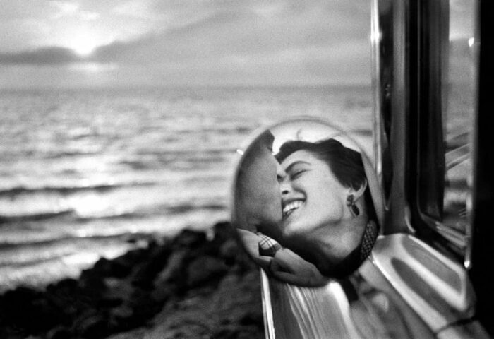 fotografía icónica del fotógrafo estadounidense Elliot Erwit donde puede verse a una pareja feliz a través del retrovisor del coche.