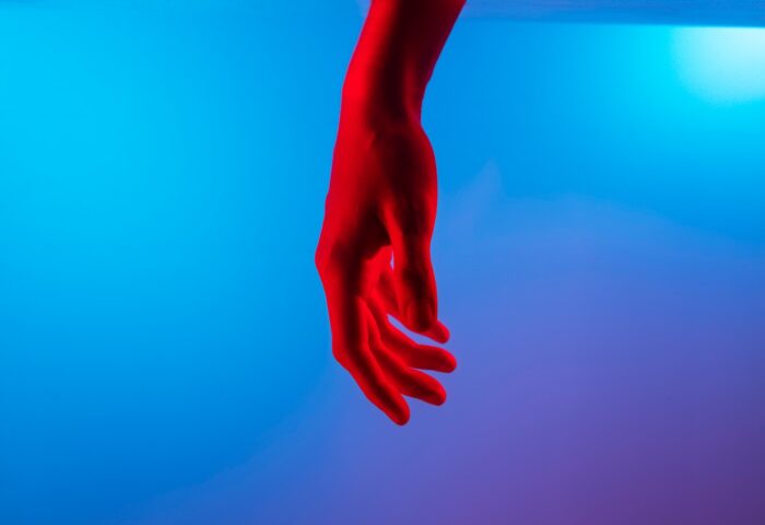 Mano roja inerte sobre fondo azul remeda el suicidio feminicida.