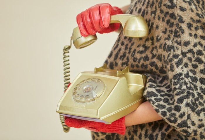 Imagen de mujer con guantes rojos levantando el auricular de un teléfono de disco.