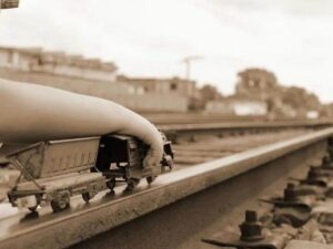 Imagen de un niño llevando un pequeño trencito de juguete por una gran línea ferroviaria.