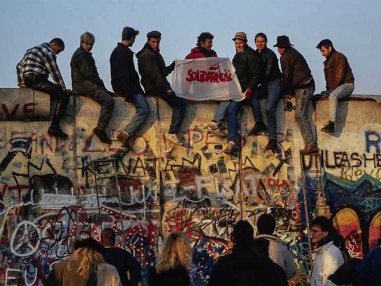 Jóvenes alemanes del este y el oeste sostienen un cartel de Solidarność sobre el Muro de Berlín. Foto: Lothar M. Peter