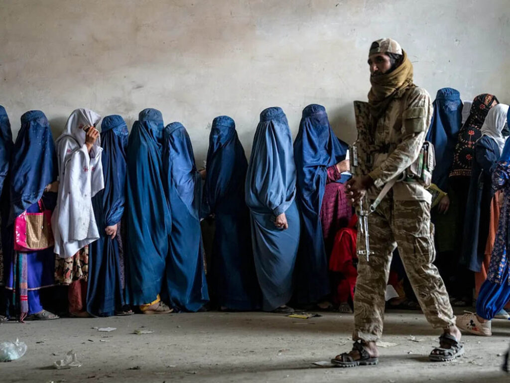 Mujeres esperan para recibir ayuda humanitaria en Kabul bajo la vigilancia de un combatiente talibán. Foto: Ebrahim Noroozi