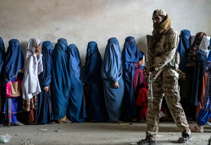 Mujeres esperan para recibir ayuda humanitaria en Kabul bajo la vigilancia de un combatiente talibán. Foto: Ebrahim Noroozi