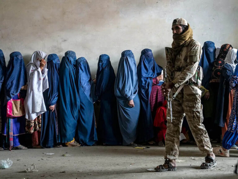 Mujeres esperan para recibir ayuda humanitaria en Kabul bajo la vigilancia de un combatiente talibán. Foto: Ebrahim Noroozi